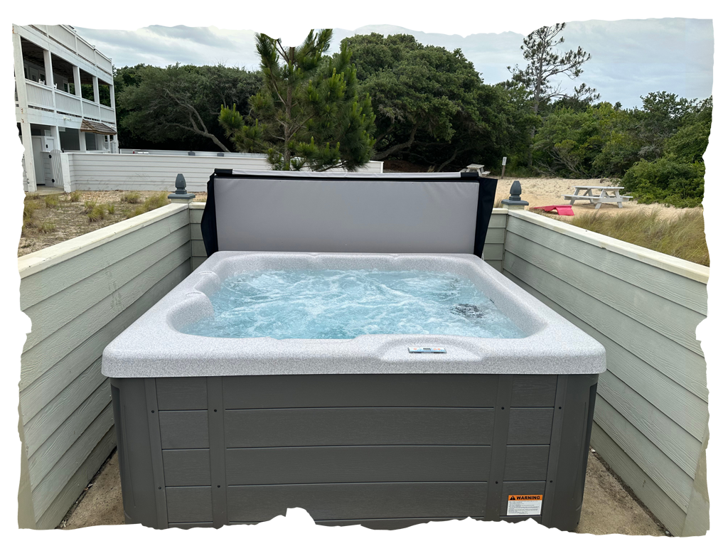 Outdoor hot tub filled with bubbling water, surrounded by a privacy fence, with trees and buildings in the background.