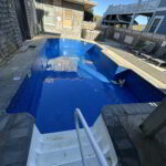 Rectangular outdoor pool with clear blue water, surrounded by a wooden deck and fenced backyard.