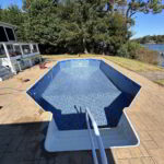 An empty above-ground pool with a blue interior and handrail, surrounded by a patio and trees.