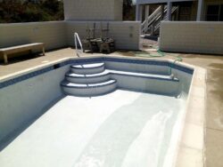 Empty swimming pool undergoing maintenance with a hose lying inside.