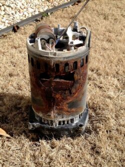 A heavily corroded and damaged outdoor air conditioning unit sitting on dry grass.
