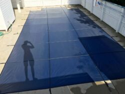 A large blue tarp laid out on the ground with the shadow of a person taking a photograph cast upon it.
