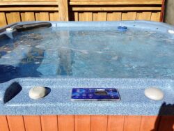 Outdoor hot tub with control panel, partially covered by water with foam bubbles on the surface.