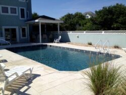 Backyard swimming pool with lounging chairs beside a two-story house.