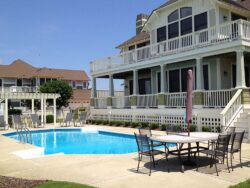 A large two-story house with a swimming pool and a patio area with seating under a clear sky.