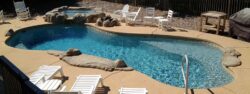 Backyard pool with lounge chairs and landscaping on a sunny day.