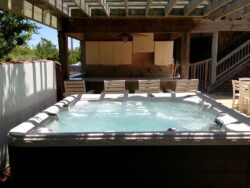 Outdoor hot tub with bubbling water, surrounded by patio furniture, adjacent to a wooden structure.