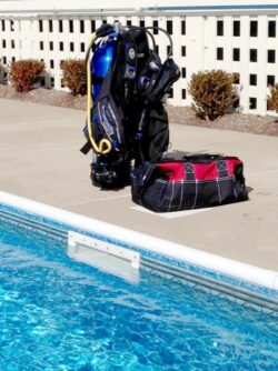 Scuba diving gear and a bag positioned beside a swimming pool.